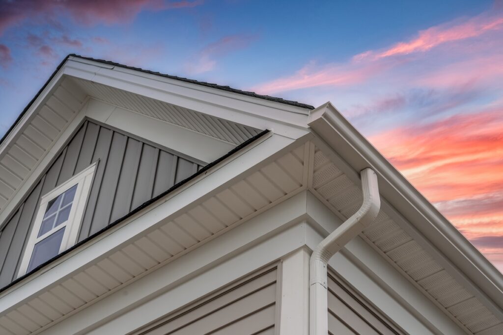 White frame gutter guard system, with gray horizontal and vertical vinyl siding fascia, drip edge, soffit, on a pitched roof attic at a luxury